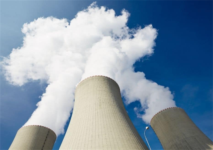 Low-angle view of steaming nuclear plant cooling towers