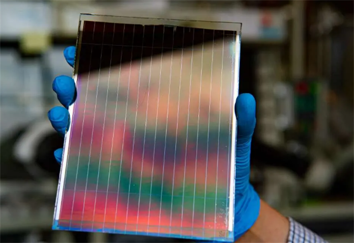 Gloved lab hand holding translucent perovskite solar cell sheet