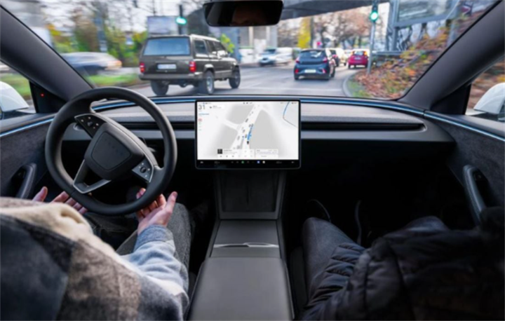 In-cabin view inside Tesla vehicle, driver’s hands near steering wheel while central touchscreen displays navigation map for FSD urban traffic testing